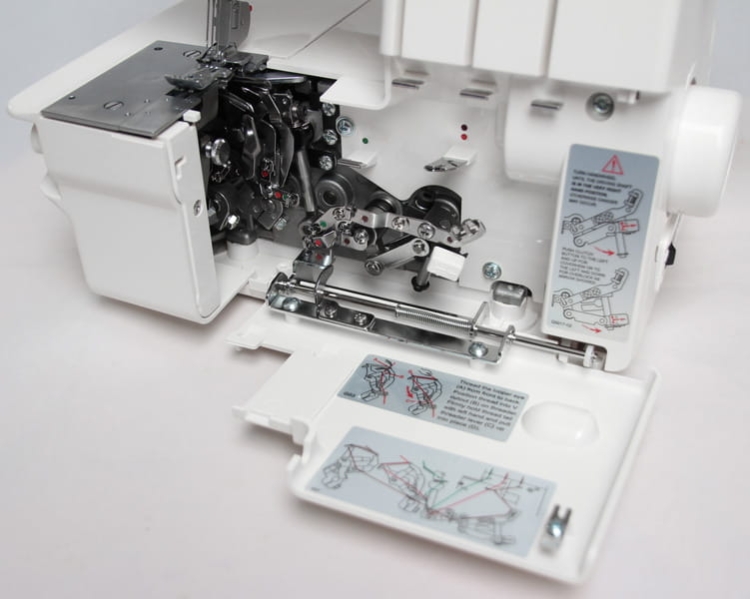 Coverlok Merrylock 689 to owerlok z funkcją renderki, ukazany z boku, z otwartą pokrywą. Widoczne mechanizmy, metalowe elementy i instrukcje obsługi na białym tle. Zestawienie detali technicznych i oznaczeń dotyczących użytkowania.