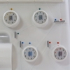 Panel kontrolny owerloka JUKI MO-644D z czterema białymi pokrętłami do regulacji naprężenia nici, z wyraźnymi numerami i kolorowymi oznaczeniami. Widoczny uchwyt oraz elementy do mocowania nici na białym tle.