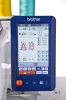 Panel sterujący hafciarki Brother VR z wyświetlaczem LCD, na którym widoczne są opcje haftu, w tym litery AB. Obok znajdują się kolorowe szpulki nici: żółta i turkusowa. Przyciski sterujące i wskaźniki postępu haftu.