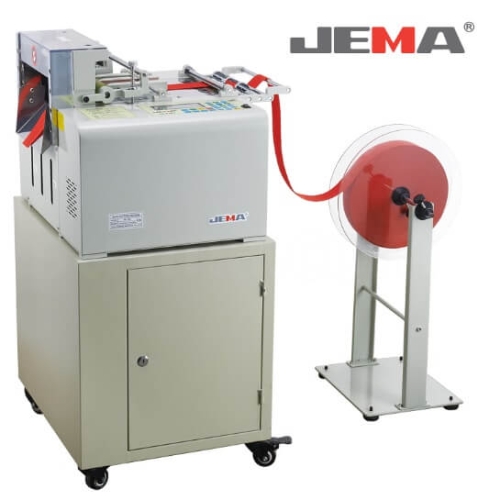 Urządzenie tnące JEMA JM-130L z automatycznym systemem, przeznaczone do cięcia średnich i grubych materiałów na zimno. Na zdjęciu widoczny jest sprzęt w kolorze szarym z czerwonymi elementami oraz stojak z rolką materiału.