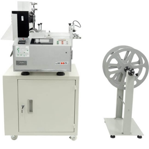 Urządzenie do cięcia taśmy JEMA JM-130LR, automatyczne, z szerokością cięcia 200 mm. Widok frontalny, produkt umieszczony na szarej podstawie z szafką, obok stojak na rolki. Panel sterujący z przyciskami i wyświetlaczem.