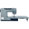 Maszyna do szycia Minerva HS1100 Heavy Duty w szarym kolorze, widok z boku. Posiada duży stół roboczy, igłę i mechanizm szyjący na widoku, z czytelnym logo Minerva. Produkt stoi na czarnej podstawie, idealny do szycia ciężkich materiałów.