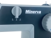 Panel sterujący maszyny do szycia Minerva HS1100 Heavy Duty, z logo Minerva. Widoczne pokrętło do regulacji oraz trzy kontrolki. Kolor szary z ciemnym tłem, z wyraźnymi oznaczeniami.