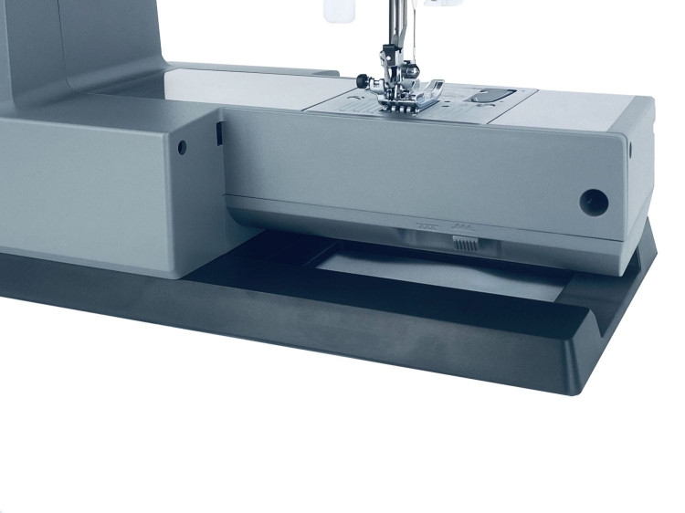 Maszyna do szycia Minerva HS1100 Heavy Duty w kolorze szarym, z widoczną stopką i uchwytem. Produkt stoi na czarnej podstawie, z detalami na panelu sterującym, w tym pokrętłem i oznaczeniami. W tle białe, jednolite tło.