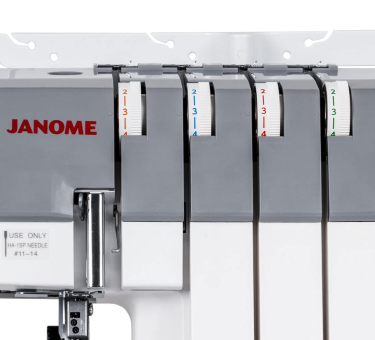 Owerlok Janome 454D z widocznymi czterema bębnami na nitki w szaro-białej obudowie. Na bębnach oznaczenia kolorowe: niebieski, czerwony, pomarańczowy i zielony. U góry logo Janome. Widok frontalny, zbliżenie na mechanizm nawlekania.