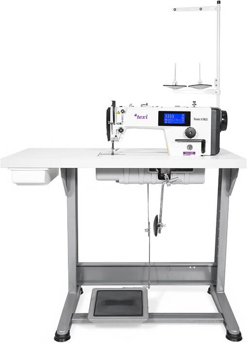 Stebnówka TEXI TRONIC 6 NEO PREMIUM 1-igłowa, umieszczona na stabilnym stole, z wyświetlaczem LCD, przeznaczona do szycia lekkich i średnich materiałów. Widoczne dwa szpulki, pedał sterujący i mechanizm transportu.