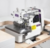 Overlock TEXI TRE 04 N PREMIUM 3-nitkowy, z widocznym metalowym blatem, panel sterujący z wyświetlaczem, białą obudową i logo texi. Maszyna stoi na stoliku, otoczona drewnianymi elementami. Wyposażona w cztery uchwyty do nici i ostrze.
