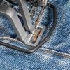 Ryglówka TEXI CATENACCIO 2.0 PREMIUM w zbliżeniu, umieszczona na niebieskim dżinsie. Widać metalowy stoper z igłą w trakcie szycia, z nicią w odcieniu brązowym. Ujęcie pokazuje detale konstrukcyjne i teksturę materiału.