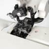 Podszywarka TEXI ACCURA 2.0 PREMIUM w zbliżeniu, ukazująca mechanizm szyjący, igłę i chwytacz. Elementy metalowe w kolorze czarnym z wyraźnymi detalami. Widoczna także część materiału oraz otwór w podłożu. Całość na jasnym tle.