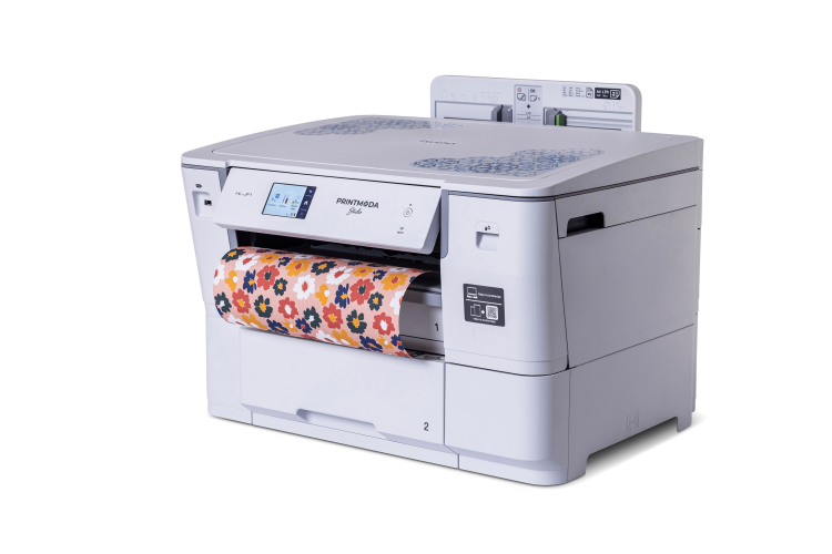 Drukarka do tkanin i papieru Brother HL-JF1 PrintModa Studio w białej obudowie, z wyświetlaczem dotykowym i kolorowym papierem w kwiatowy wzór, umieszczona w pozycji stojącej, z widocznym podajnikiem papieru i wyjściem.
