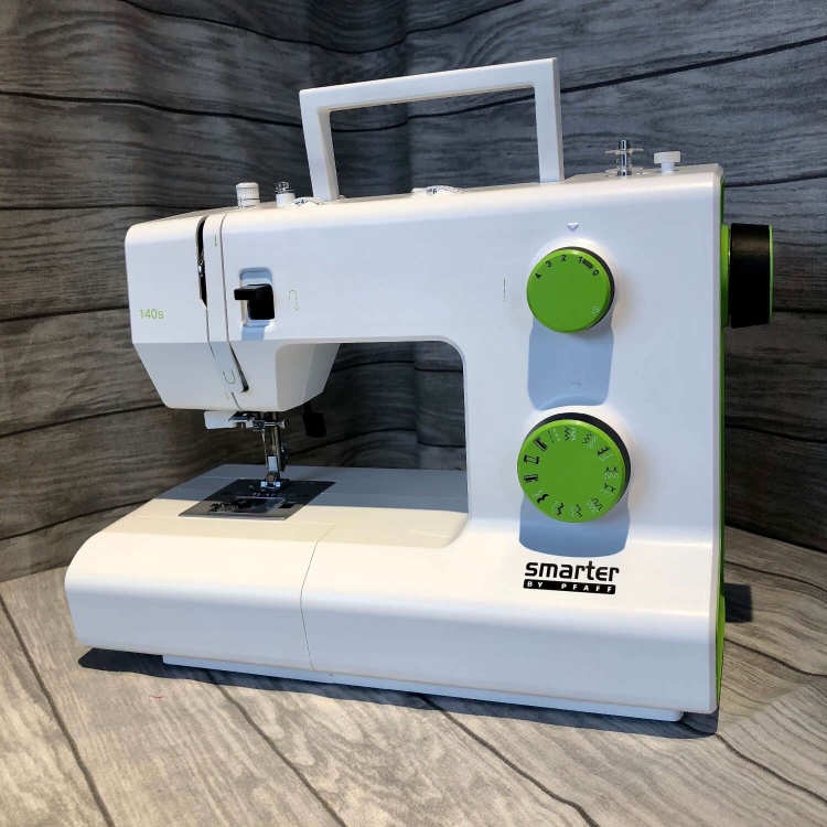 Maszyna do szycia PFAFF SMARTER 140S w kolorze białym z zielonymi pokrętłami, stojąca w ujęciu z boku. Widoczny mechanizm szycia, numer modelu 140S oraz logo smarter by PFAFF na obudowie.