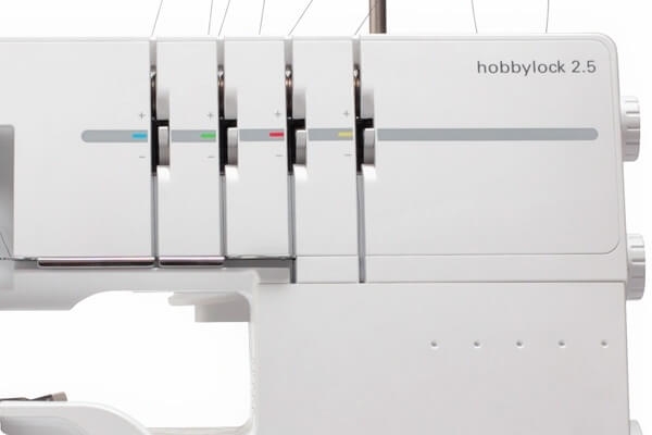 Owerlok PFAFF HOBBYLOCK 2.5 w kolorze białym, z widocznymi pokrętłami i oznaczeniami dla czterech nitek. Ujęcie frontalne, zbliżenie na panel sterujący z kolorowymi wskaźnikami i logo hobbylock 2.5.