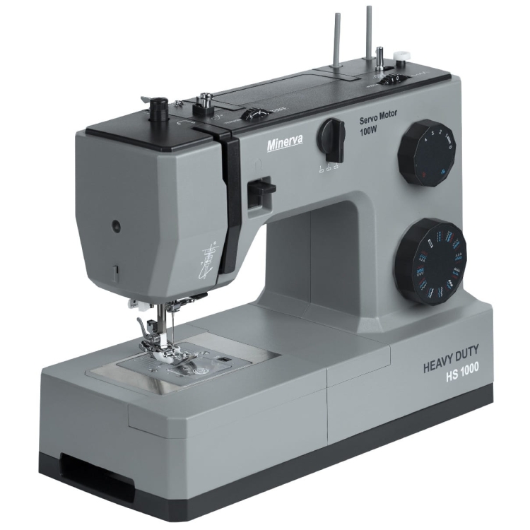 Maszyna do szycia Minerva HS1000 w kolorze szarym, z mechaniczną konstrukcją. Widoczny stół do szycia, pokrętła regulacyjne oraz logo. Kąt ujęcia z boku, prezentujący detale maszyny i jej funkcje.