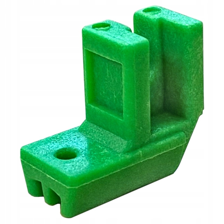 Plastikowa stopka do zamków błyskawicznych w intensywnym zielonym kolorze. Produkt ma kształt litery L z dwoma otworami montażowymi. Widoczna faktura powierzchni jest gładka, a stopka jest ustawiona w pozycji leżącej.