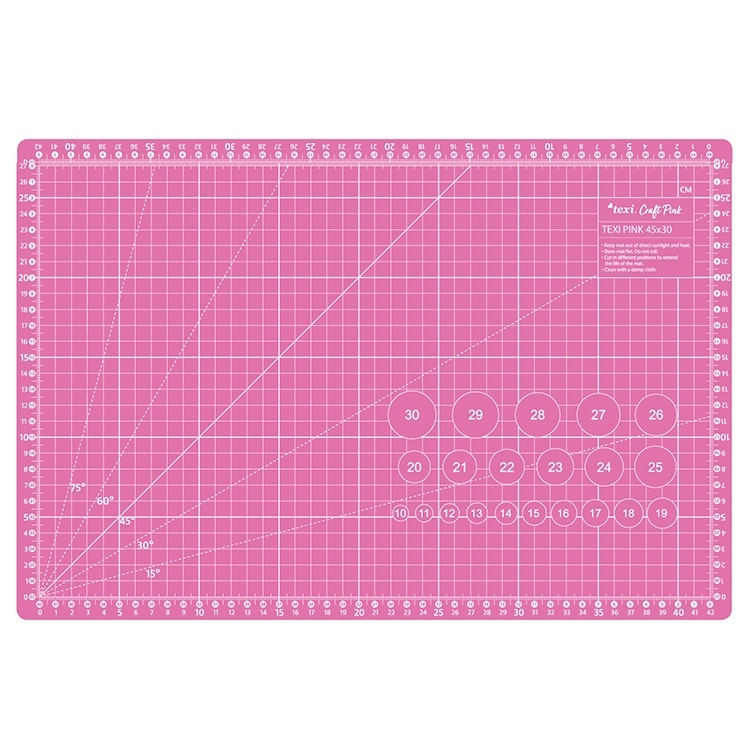 Różowa mata podkładowa TEXI PINK 45x30 cm, samoregenerująca, z siatką w centymetrach oraz kątami, widoczne oznaczenia dla precyzyjnego cięcia, leżąca na prostym tle.