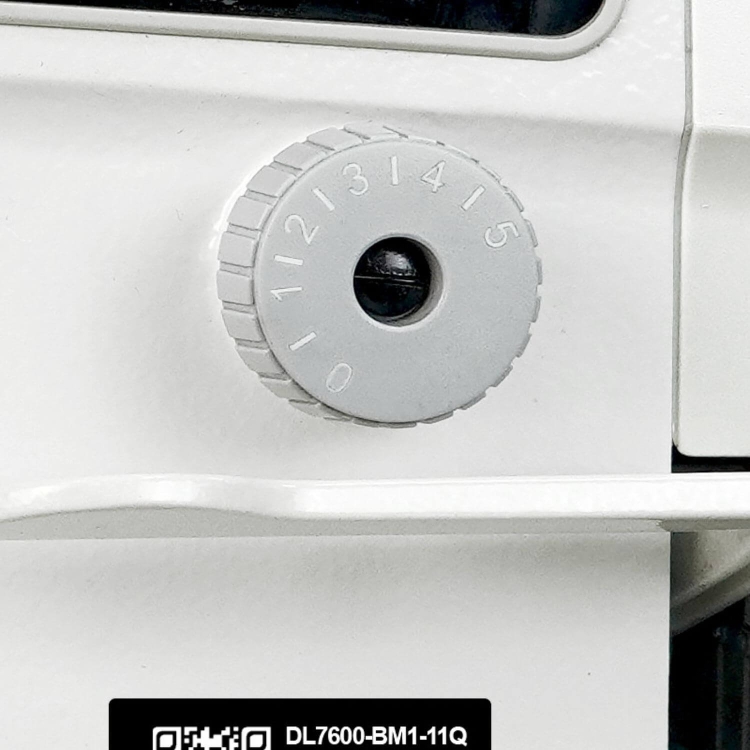 Regulator na obudowie stebnówki SIRUBA DL7600-BH1-11Q, wykonany w kolorze szarym, z oznaczeniami od 0 do 15. Widoczny jest również czarny element w środku. Tło proste, białe, z logo w dolnej części.