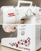Maszyna do szycia Janome JUNO E1015 w kolorze białym z czerwonym logo. Widoczne pokrętła do regulacji i wzory kwiatowe na obudowie. Ujęcie z boku i z przodu, pokazujące igłę oraz miejsce na szpulkę. Idealna do szycia na różne materiały.