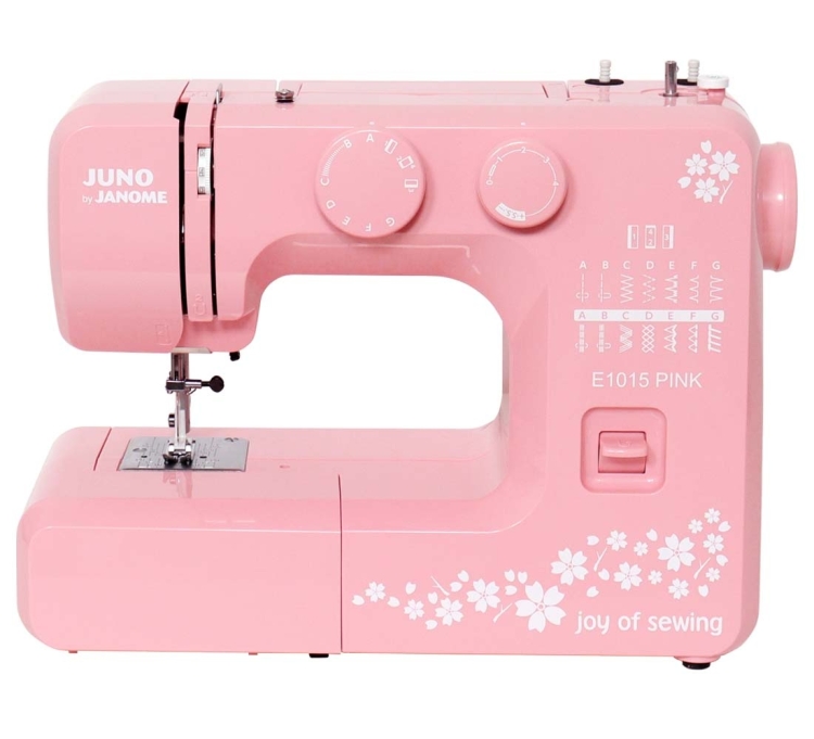 Maszyna do szycia Janome JUNO E1015 w kolorze różowym, z białymi zdobieniami i napisem joy of sewing. Widok z boku, z widocznymi pokrętłami do ustawień, miejscem na igłę oraz tkaniną. Idealna dla początkujących.