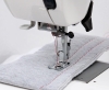 Maszyna do szycia Janome HD 523 EASY JEANS, widok z bliska na stopkę oraz igłę szyjącą, z szarym materiałem z widocznym czerwonym ściegiem. Elementy maszyny są w kolorze białym i metalicznym, z ergonomicznym uchwytem oraz pedałem.