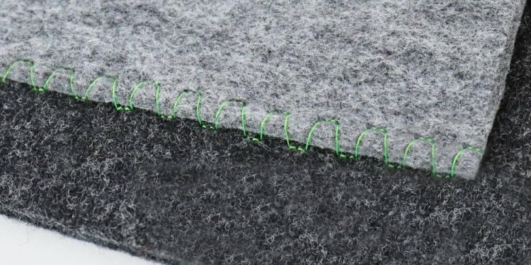 Zbliżenie na dwa kawałki szarego filcu, jeden jasny, drugi ciemny, połączone zielonym ściegiem. Widoczna faktura materiału, który jest gładki i włóknisty. Idealne do zastosowań w szyciu i rzemiośle.
