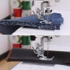 Maszyna do szycia Janome HD 523 EASY JEANS z widoczną stopką, szyjąca grube materiały, takie jak dżins i skóra. Ujęcie z bliska, ukazujące detal szycia na dwóch warstwach tkanin. Tło z szpulkami nici w różnych kolorach.
