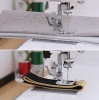 Maszyna do szycia Janome HD 523 EASY JEANS w zbliżeniu, pokazująca stopkę do szycia na dwóch rodzajach materiałów: szarym i czarnym z beżowym. Widoczne nitki, a w tle kolorowe szpule z nicią.