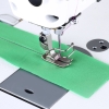 Stebnówka TEXI TRONIC 7HF NF PREMIUM EX z widoczną igłą i stopką, szyjąca zielony materiał. W tle srebrna płyta maszyny. Ujęcie z bliska na detal szycia, z widoczną nicią w kolorze różowym.