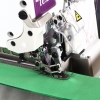 Maszyna owerlok TEXI QUATTRO 1F PREMIUM EX, 4-nitkowa, w zbliżeniu na stopkę i mechanizm szyjący. Widoczna zielona tkanina oraz różowe szwy. Metalowa konstrukcja z przezroczystą osłoną. Ujęcie z prawej strony, podkreślające detale robocze.