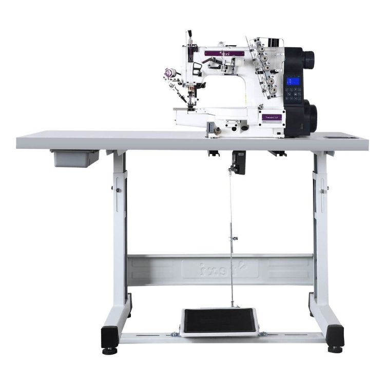 Renderka TEXI TRECCIA-C 3F PREMIUM EX w kolorze białym, z trzema igłami i interlokiem. Ustawiona na stabilnym stole, wyposażona w pedal do sterowania oraz pojemnik na akcesoria. Elektroniczny panel sterujący z wyświetlaczem.