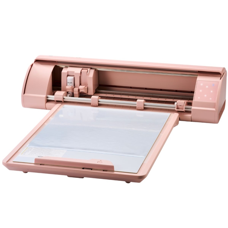 Ploter tnący Silhouette CAMEO5a w kolorze różowym, z widoczną dużą matą do cięcia. Produkt leży otwarty, ukazując wnętrze z głowicą tnącą oraz przyciskami. Na matę nałożony jest arkusz materiału.