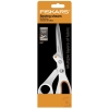 Nożyce krawieckie Fiskars Amplify 1070082 o długości 25 cm, z metalowymi ostrzami i ergonomicznym uchwytem w kolorze białym z pomarańczowymi akcentami, umieszczone na tle opakowania z informacją o możliwości cięcia wielu warstw materiału.