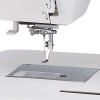 Hafciarka Janome MC500E LE z programem Artistic Digitizer JR, zbliżenie na igłę i haftowany wzór kwiatów w pastelowych kolorach na niebieskim tle. Widoczne przyciski sterujące: START/STOP oraz nożyczki.