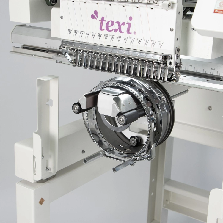 Hafciarka TEXI 1501 XL TS PREMIUM SET, przemysłowa, 15-igłowa. Zbliżenie na mechanizm z przodu maszyny z chromowanymi elementami, w tym ramieniem i rolkami, na białym tle, ukazującym detale konstrukcyjne i precyzyjne wykonanie.