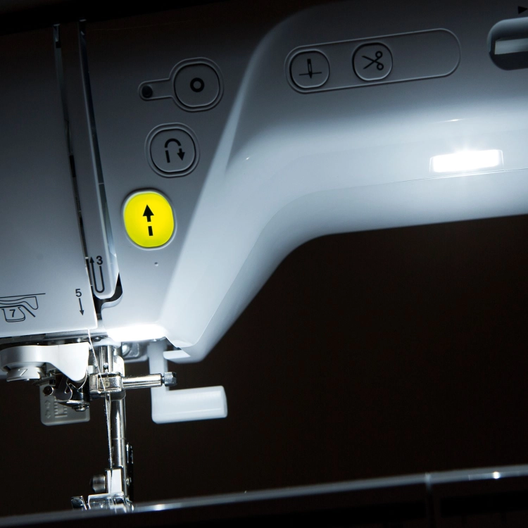 Maszyna do szycia Brother NV1040 SE w białej obudowie z czerwonymi detalami. Wyposażona w panel sterujący z wyświetlaczem LCD oraz przyciskami do wyboru ściegów. Widoczne przyrządy do szycia i podziałka na obudowie. Z przodu widoczny stół roboczy.