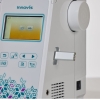 Maszyna do szycia Brother F560 w kolorze białym z kolorowym wyświetlaczem LCD. Widoczny panel sterujący z przyciskami, w tym ikonami funkcji i portem USB. Ujęcie z boku, ukazujące detale konstrukcyjne i logo Innov-is.