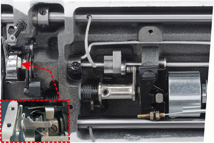 Zbliżenie na mechanizm stebnówki JACK A2C-CH, jednoigłowej z automatycznym obcinaniem nici. Widoczne elementy metalowe, w tym silnik oraz mechanizmy sprężynowe, z wyraźnym zaznaczeniem części odpowiedzialnej za obcinanie nici. Tło w kolorze szarym.