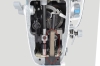 Widok wewnętrzny stebnówki JACK A6F-E, ukazujący mechanizm z transportem ząbkowo-igłowym. Widoczne elementy metalowe prowadnice, sprężyny oraz zębatki, które odpowiadają za automatyczne przesuwanie materiału. Całość w kolorze srebrnym z detalami czarnymi