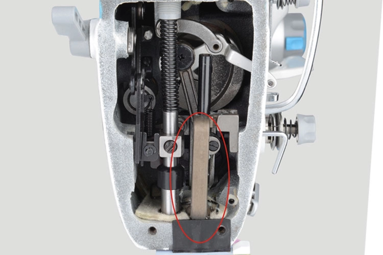 Widok wewnętrzny stebnówki JACK A6F-E, ukazujący mechanizm z transportem ząbkowo-igłowym. Widoczne elementy metalowe prowadnice, sprężyny oraz zębatki, które odpowiadają za automatyczne przesuwanie materiału. Całość w kolorze srebrnym z detalami czarnymi