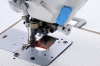 Zdjęcie pokazuje zbliżenie obszaru roboczego przy igle i odkrawaczu bocznym. Czerwona strzałka z oznaczeniem 26 mm wskazuje odległość pomiędzy stopką maszyny a krawędzią otworu w płytce roboczej.