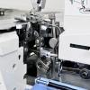 Zbliżenie na chwytacze, nóż i metalowe podzespoły owerloka Minerva AutoFlow Z-One. Fotografia pokazuje precyzyjny mechanizm odpowiedzialny za tworzenie ściegu, obcinanie zapasu i zabezpieczanie krawędzi.