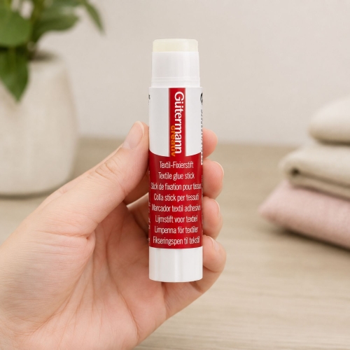 Klej do tkanin Gutermann Creativ Textile Glue Stick pokazany pionowo na czystym, białym tle. Fotografia dokładnie prezentuje czerwono-białe opakowanie, etykietę produktu oraz kompaktową formę praktycznego sztyftu.