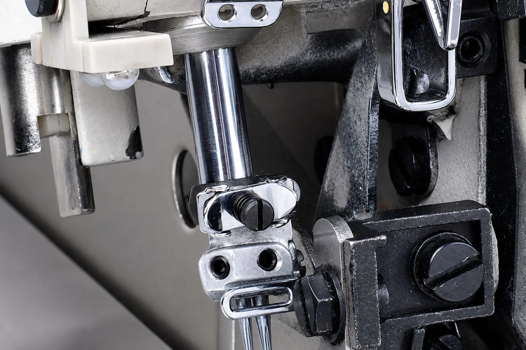 Zbliżenie na mechanizm owerloka JACK JK-798TDI-4-514-A04/435, ukazujące metalowe elementy, takie jak chromowane rury, śruby oraz dźwignie. Widoczna jest także część obudowy maszyny oraz elementy mocujące, w tym czarne pokrętło regulacyjne.