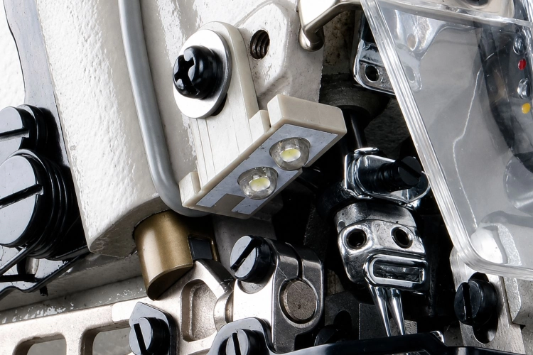 Zbliżenie na mechanizm owerloka JACK JK-798TDI-5-516-A04/435, ukazujące metalowe elementy, plastikowe przyciski oraz diody LED. Widoczne śruby i mocowania w kolorze czarnym oraz srebrnym, z częściowo przezroczystą osłoną.