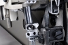 Zbliżenie na mechanizm owerloka JACK JK-798TDI-5-516-A04/435, ukazujące metalowe elementy, śruby i mocowania. Widoczny chromowany pręt i czarne przyciski. Tło neutralne, co podkreśla detale konstrukcji maszyny.