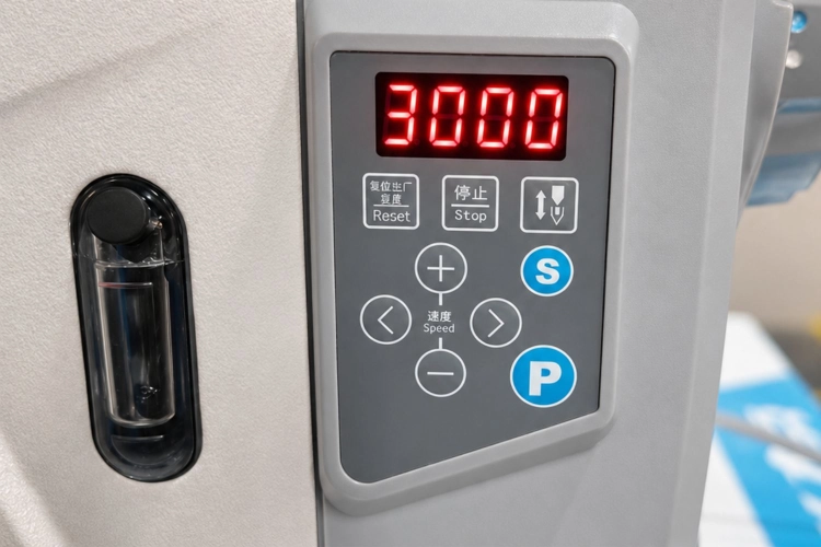 Zdjęcie przedstawia elektroniczny panel sterowania wbudowany w głowicę maszyny. Wyświetlacz pokazuje ustawioną prędkość, a przyciski pozwalają zmieniać parametry pracy i korzystać z funkcji pozycjonowania igły.