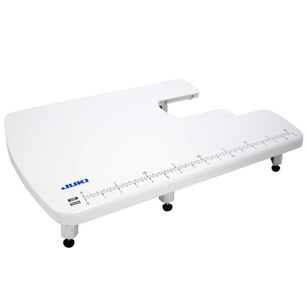 Stolik powiększający pole robocze JUKI seria HD w kolorze białym, z wycięciem i podziałką w centymetrach. Ustawiony poziomo, z regulowanymi nóżkami dla stabilności. Widoczne logo JUKI.