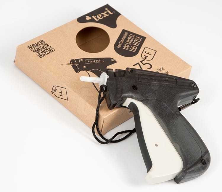 Pistolet do etykietowania Texi 75F GUN fine w kolorze czarno-białym, z widoczną rękojeścią i przyciskiem. Obok znajduje się opakowanie kartonowe z okrągłym otworem oraz grafiką produktu. Produkt leży na białym tle.