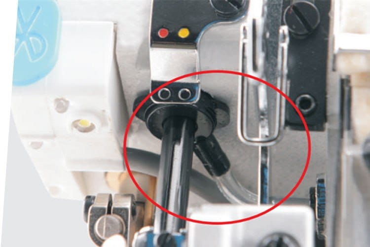 Zbliżenie na elementy mechaniczne owerloka JACK C5F-3-32R2/223, ukazujące czarną rurkę oraz metalowy uchwyt z widocznymi oznaczeniami. Ujęcie pod kątem, na jasnym tle, prezentujące detale konstrukcyjne maszyny do szycia.