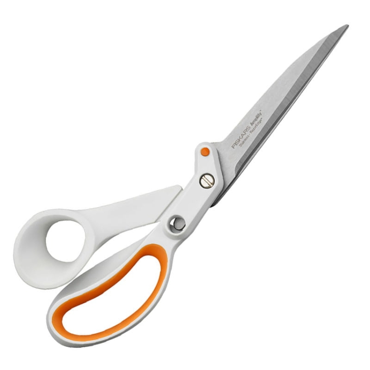 Nożyce krawieckie Fiskars Amplify 1070082 o długości 25 cm, z ostrzami ze stali nierdzewnej. Ergonomiczne uchwyty w białym kolorze z pomarańczowymi akcentami, stojące w pozycji otwartej, idealne do precyzyjnego cięcia materiałów.