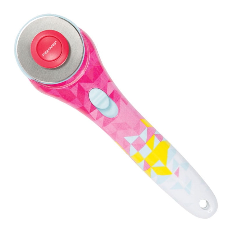 Nóż krążkowy Fiskars Inspiration Geometric 1023908 o średnicy 45 mm, z ergonomiczną rączką w różowo-żółte wzory geometryczne, metalową ostrza, z czerwonym przyciskiem i niebieskim włącznikiem, ujęty z boku na białym tle.